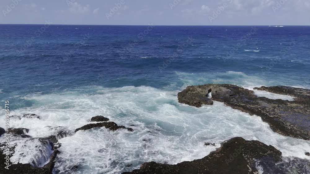 Drone flies backwards as waves chase the drone, crashing against a small rocky island Drone flies backwards as waves chase the drone, crashing against a small rocky island