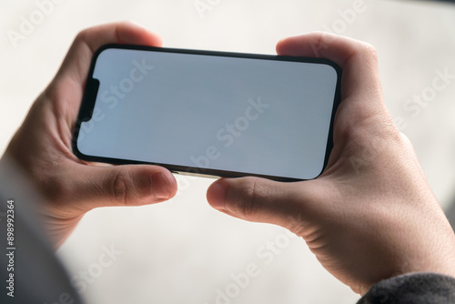 Young man hands holding smartphone horizontally with blank white screen.