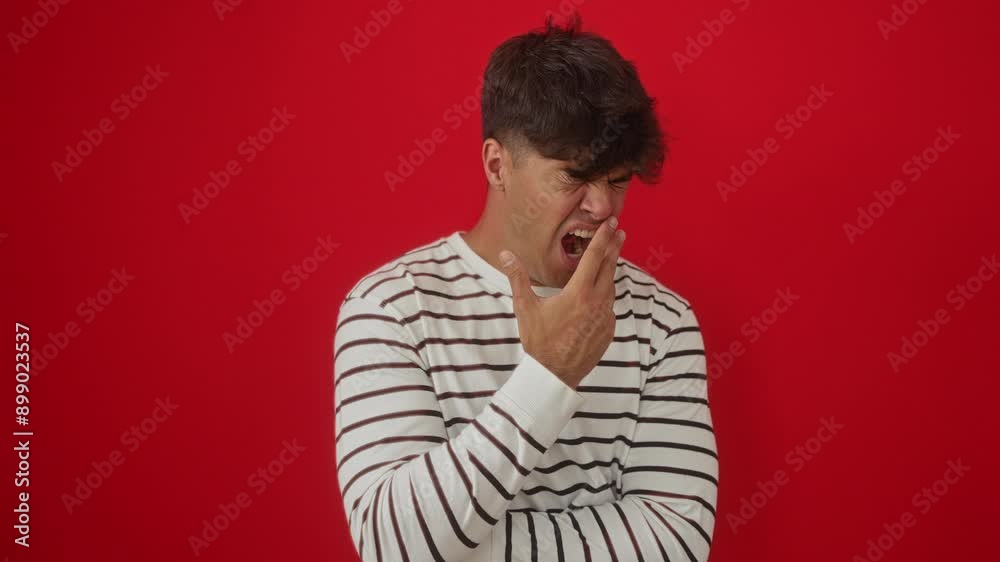 Yawning young hispanic man wearing stripes t shirt standing tired and bored with hand over mouth in a state of sleepiness against isolated red background Yawning young hispanic man wearing stripes t shirt standing tired and bored with hand over mouth in a state of sleepiness against isolated red background