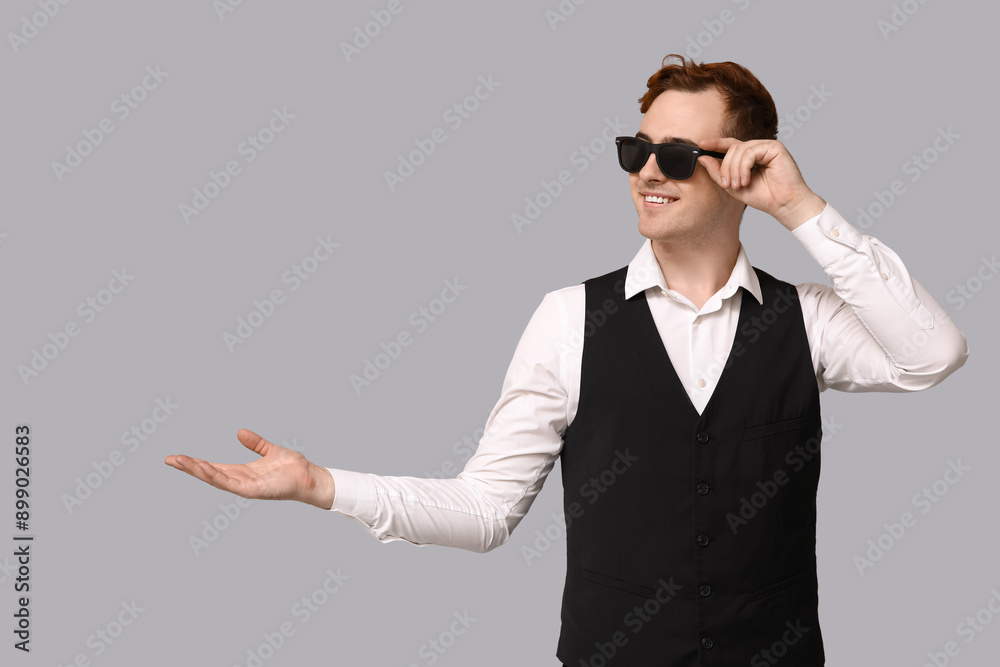Young man in sunglasses pointing at something on grey background. Black Friday sale Young man in sunglasses pointing at something on grey background. Black Friday sale