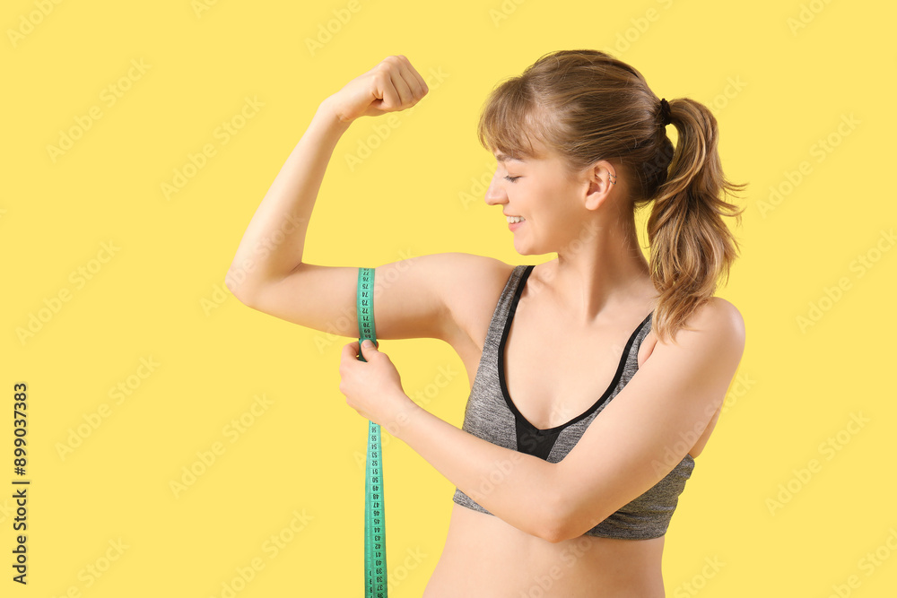 Beautiful young sporty woman measuring her biceps on yellow background. Weight loss concept Beautiful young sporty woman measuring her biceps on yellow background. Weight loss concept
