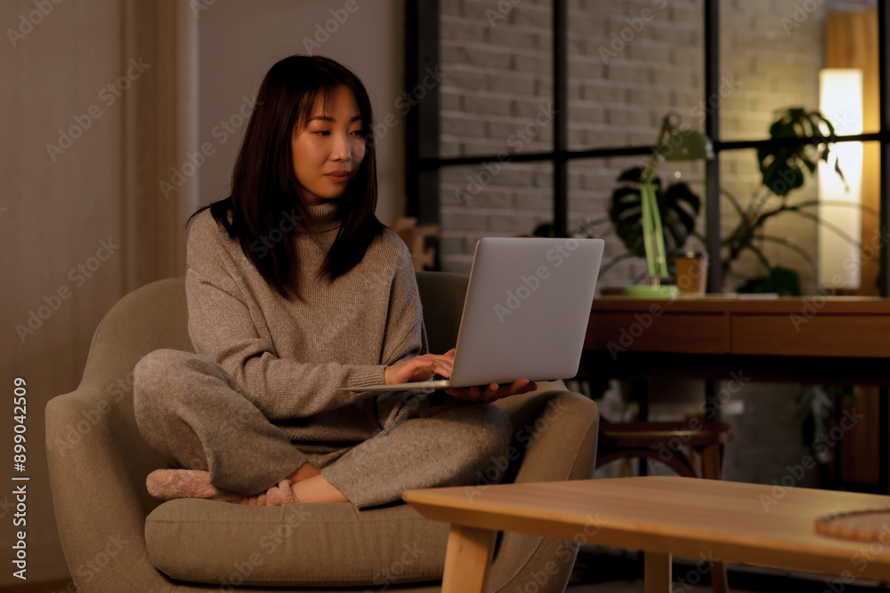 Young Asian woman in pajamas with laptop sitting on armchair Young Asian woman in pajamas with laptop sitting on armchair