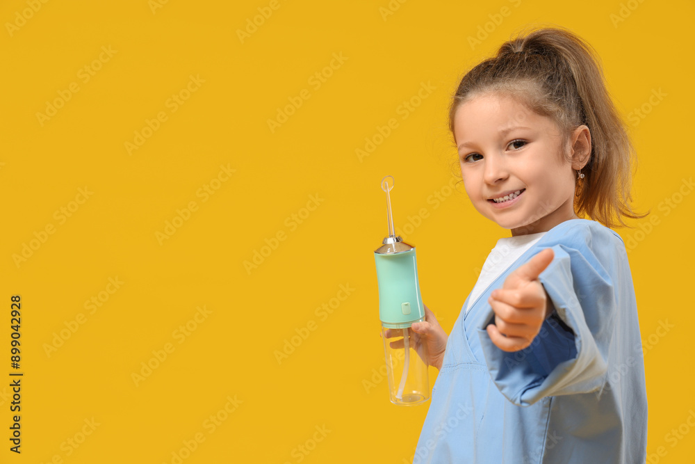 Cute little girl with oral irrigator showing thumb-up gesture on yellow background Cute little girl with oral irrigator showing thumb-up gesture on yellow background