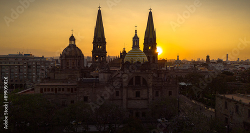 A breathtaking aerial panoramic view of Guadalajara, Mexico, during a spectacular sunset. The majestic sun sets on the horizon, with the city's iconic cathedral and its distinctive yellow domes promin