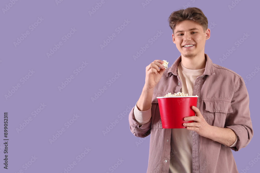 Handsome young man holding bucket with popcorn on lilac background Handsome young man holding bucket with popcorn on lilac background