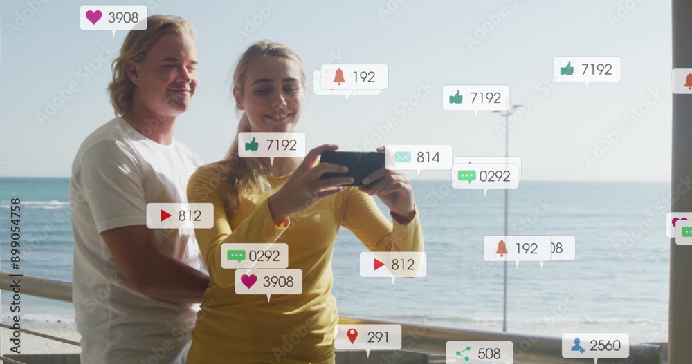Obraz premium Social media notifications image over couple taking selfie by sea