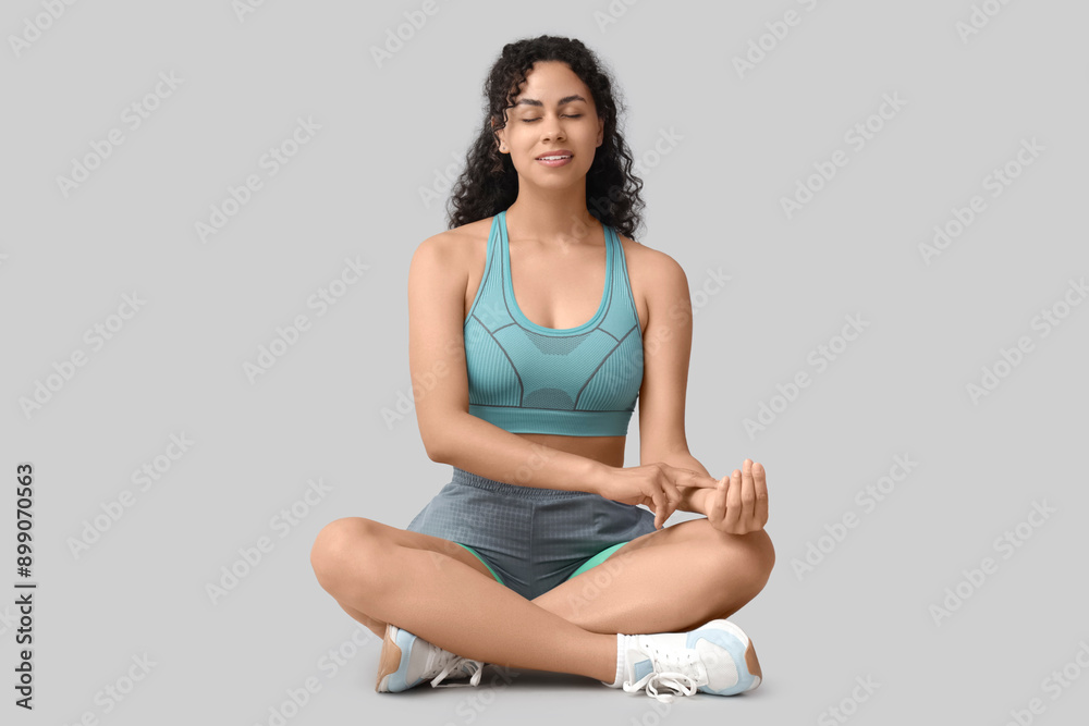 Sporty African-American woman checking pulse on grey background Sporty African-American woman checking pulse on grey background