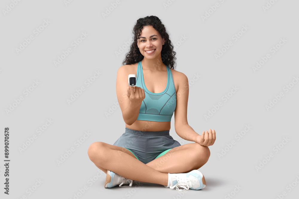 Sporty African-American woman checking pulse on grey background Sporty African-American woman checking pulse on grey background