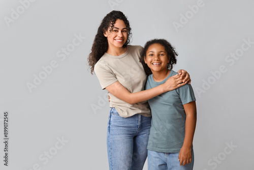 Beautiful young happy African-American mother with her daughter hugging on grey background © Pixel-Shot