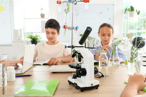 Modern microscope on table and pupils studying in Biology class at school, closeup