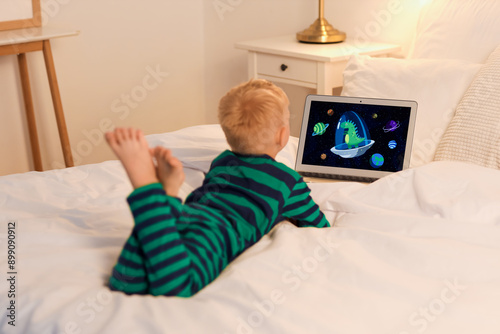 Cute little boy watching cartoons on laptop in bedroom at night, back view