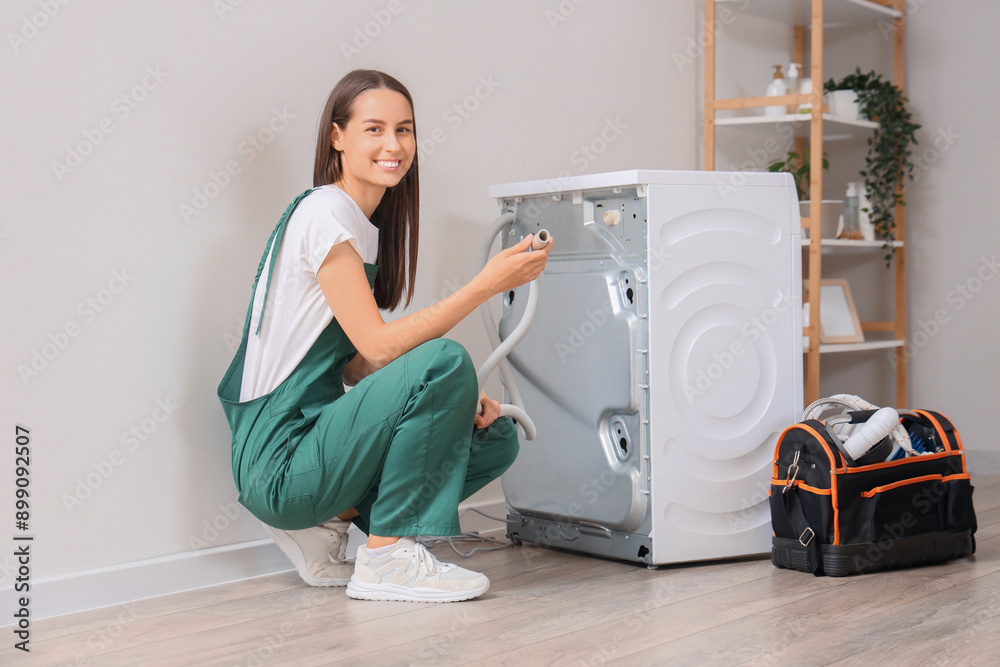 Female plumber fixing washing machine in bathroom Female plumber fixing washing machine in bathroom