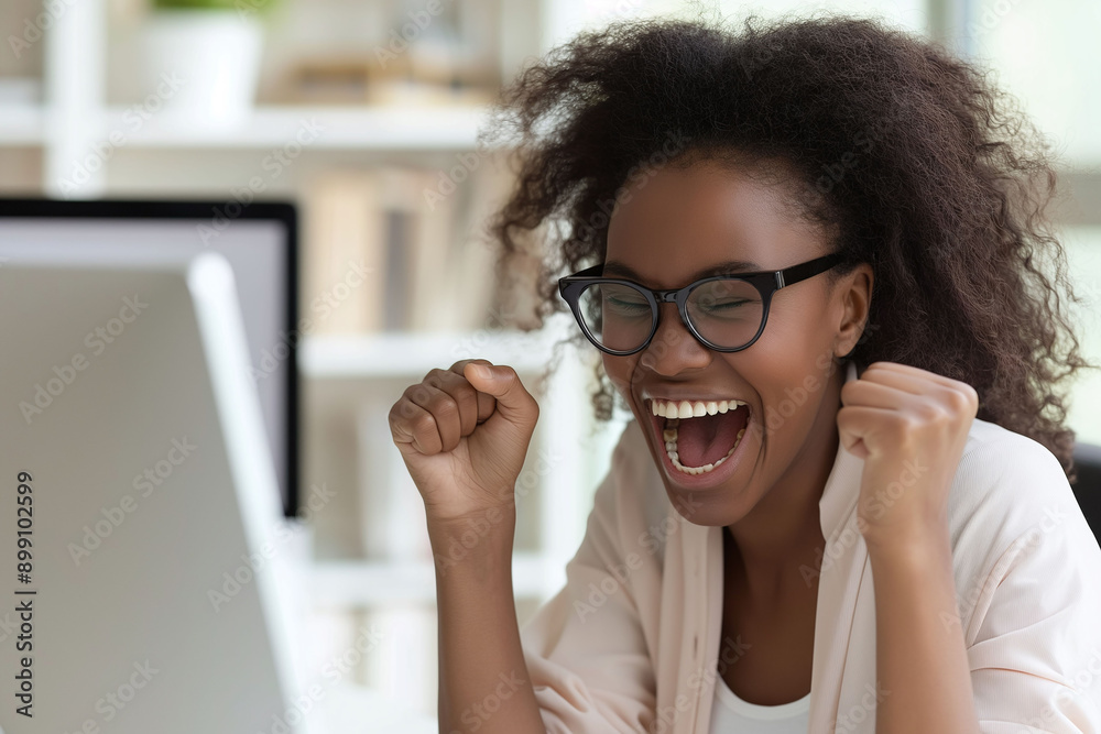 An excited young African American woman with glasses and curly hair celebrates with her laptop in a modern indoor environment. An excited young African American woman with glasses and curly hair celebrates with her laptop in a modern indoor environment.
