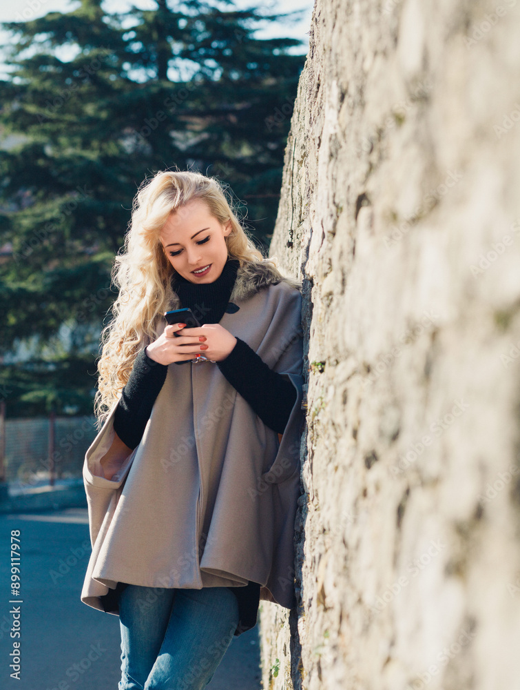 Young woman using smartphone app leaning on stone wall in europe Young woman using smartphone app leaning on stone wall in europe