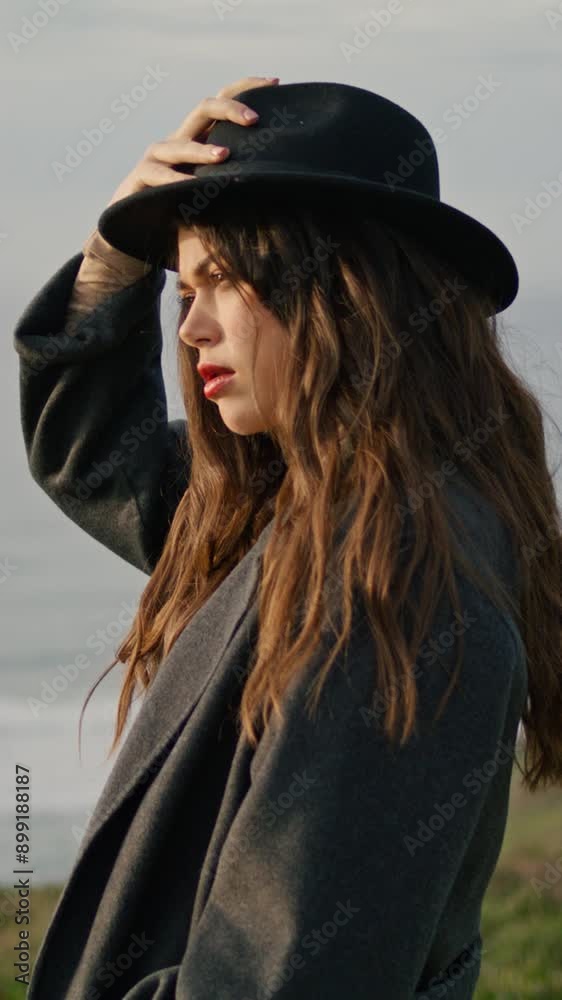 Model posing holding hat at ocean coast evening vertical closeup. Serious woman Model posing holding hat at ocean coast evening vertical closeup. Serious woman