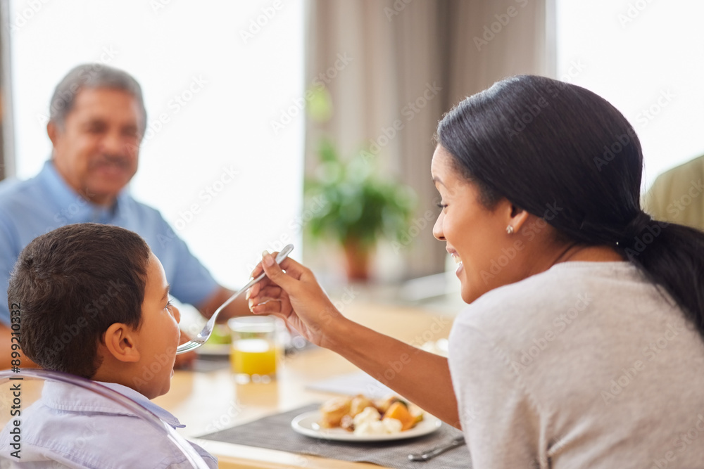 Family, food and mother feeding son at dining room table in home for meal or social gathering. Breakfast, eating and help with happy people in apartment together for bonding, diet or nutrition Family, food and mother feeding son at dining room table in home for meal or social gathering. Breakfast, eating and help with happy people in apartment together for bonding, diet or nutrition