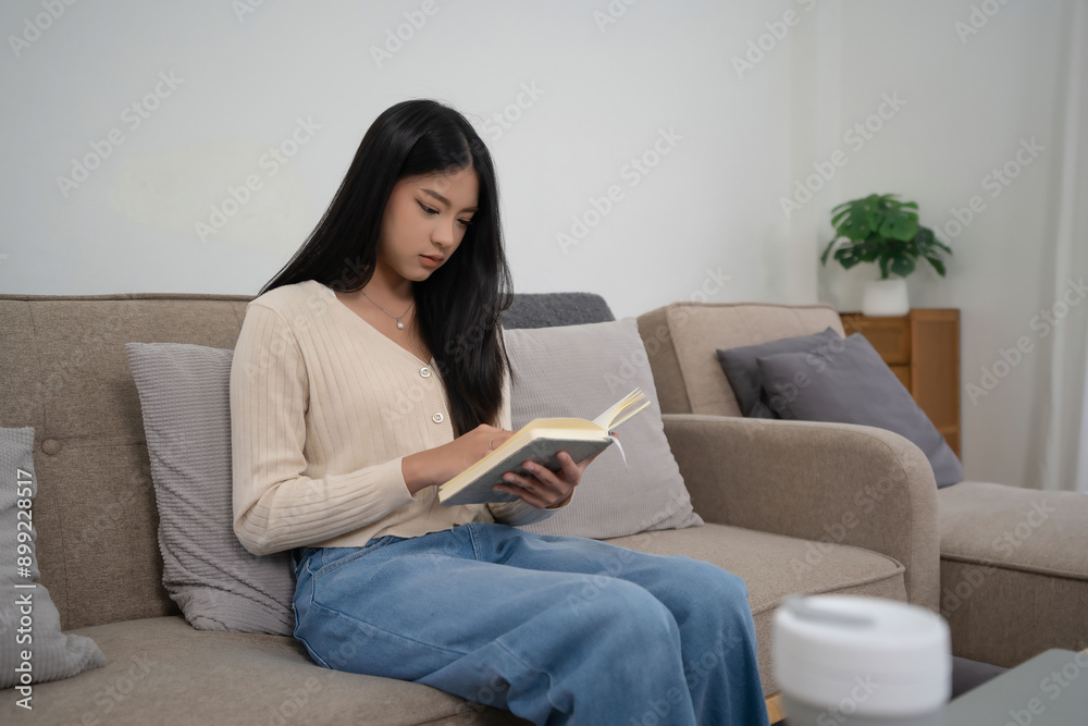 Young asian women reading a book to studying and researching educational while sitting on comfortable couch to learning self-study and spending time to relaxation with enjoying lifestyle at home Young asian women reading a book to studying and researching educational while sitting on comfortable couch to learning self-study and spending time to relaxation with enjoying lifestyle at home