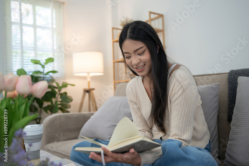 Young asian women reading a book to studying and researching educational while sitting on comfortable couch to learning self-study and spending time to relaxation with enjoying lifestyle at home