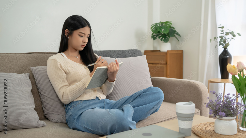 Young asian women reading a book to researching educational and taking notes while sitting on comfortable couch to learning self-study and spending time to relaxation with enjoying lifestyle at home Young asian women reading a book to researching educational and taking notes while sitting on comfortable couch to learning self-study and spending time to relaxation with enjoying lifestyle at home