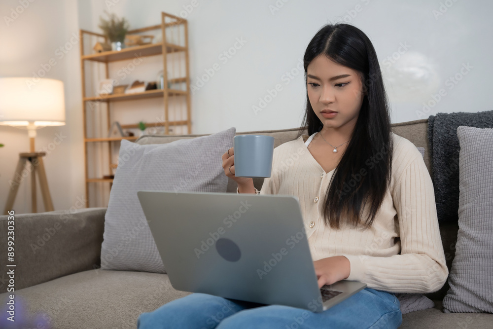 Fototapeta premium Young asian women putting laptop on legs to typing marketing report of business project and holding cup of hot coffee to drinking beverage while spending time and relaxation with enjoying lifestyle