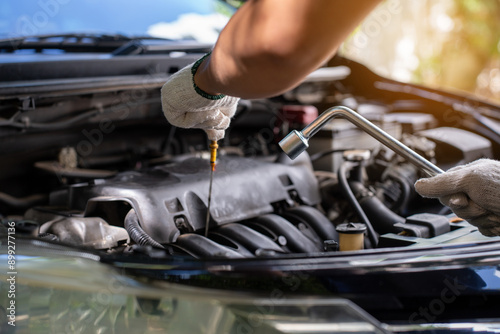 Close-up of Car mechanic noting repair parts during open car hood engine repair unrecognisable man wearing gray glove inspecting car engine and interior of hood of car. at garage