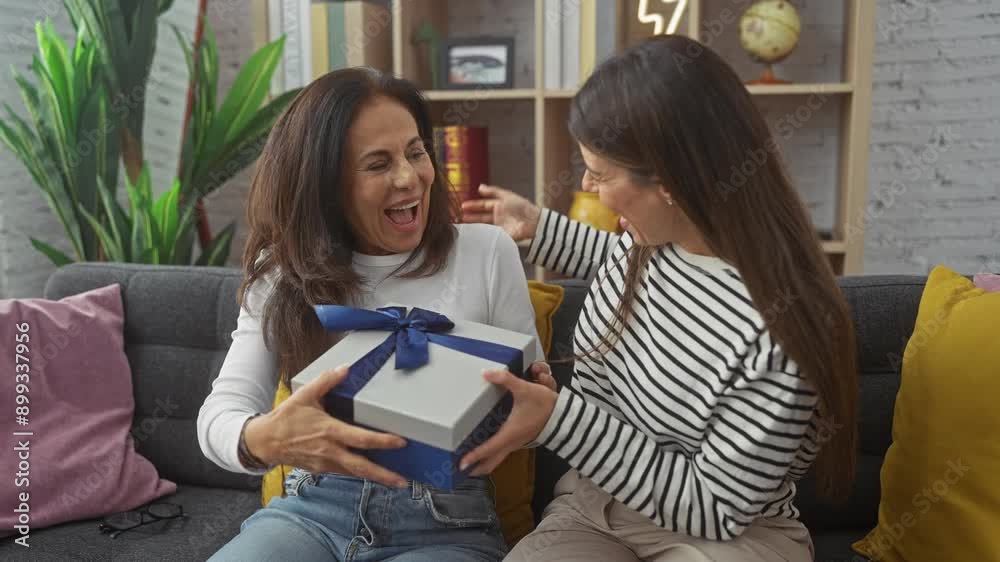 A smiling woman surprises her mother with a gift box in a cozy living room, expressing love and family bond. A smiling woman surprises her mother with a gift box in a cozy living room, expressing love and family bond.