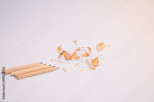 A pile of pencil shavings sits on a white surface next to four pencils. The pencils are all different colors, and the shavings are scattered all over the surface