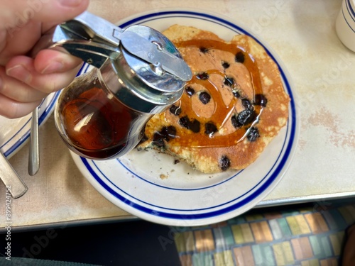 Hand pouring syrup over blueberry pancake on diner plate photo