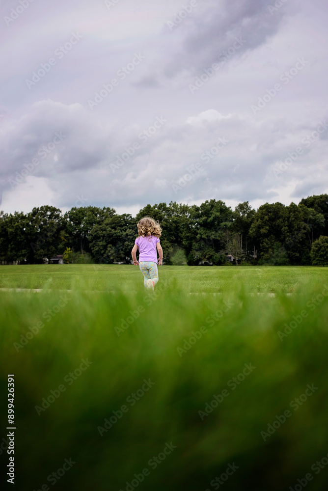 Young girl running through field of grass from behind