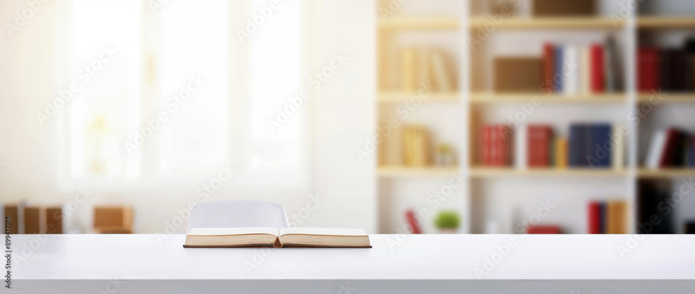 Open book on a white desk with a blurred home office background with a bookcase full of books