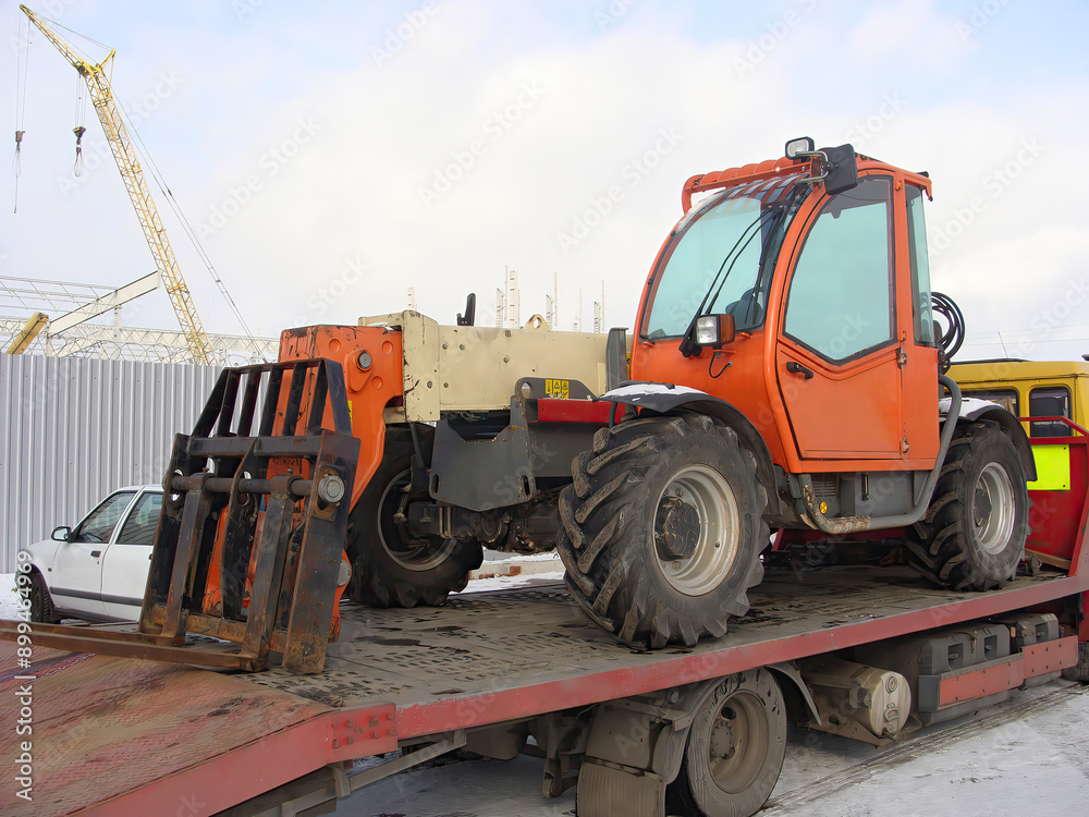 Orange forklift on a flatbed truck, ready for transportation at a construction site. Orange forklift on a flatbed truck, ready for transportation at a construction site.