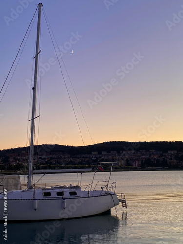 Boat with a sunset in the background and a moon by the sea.