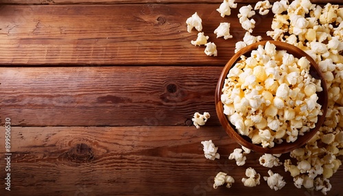 A bowl of delicious popcorn and some are scattered below on a wooden background. Wallpapers.