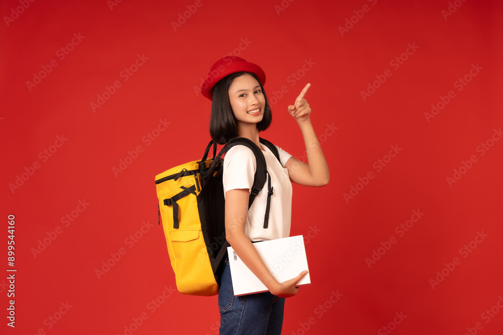 Asian female student looks at the studio with red background reflecting her dedication to learning, where education leads to her knowledge and intelligence, carrying a yellow bag and holding books. Asian female student looks at the studio with red background reflecting her dedication to learning, where education leads to her knowledge and intelligence, carrying a yellow bag and holding books.