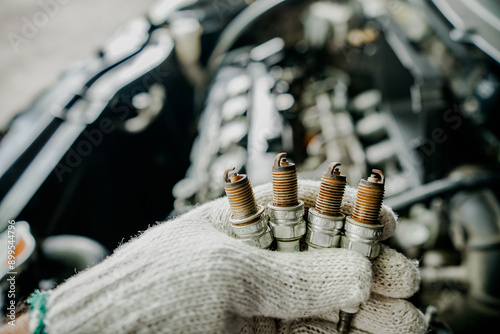 Close-up of an auto mechanic's hand holding a used spark plug removed from a car. Old used spark plug in the hand of a gloved man in a car service center. Concept car maintenance