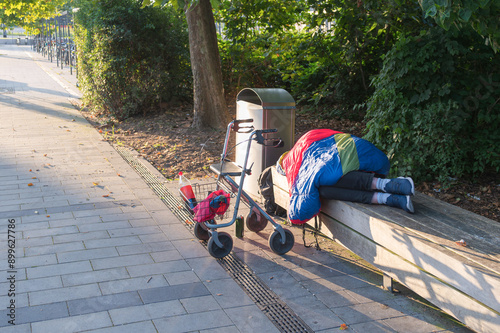 Ein Obdachloser schläft auf einer Parkbank , davor sein Rollator photo