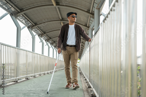 Young blind man walking in city with walking stick. Visually impaired man difficult to traveling on the road wearing sun glasses Cross the road cross the footbridge photo