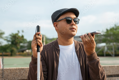 Obraz na płótnie Young asian blind man using application on mobile phone to helping accessibility for persons with visual impairment. Technology for blind people sending voice message or navigation.