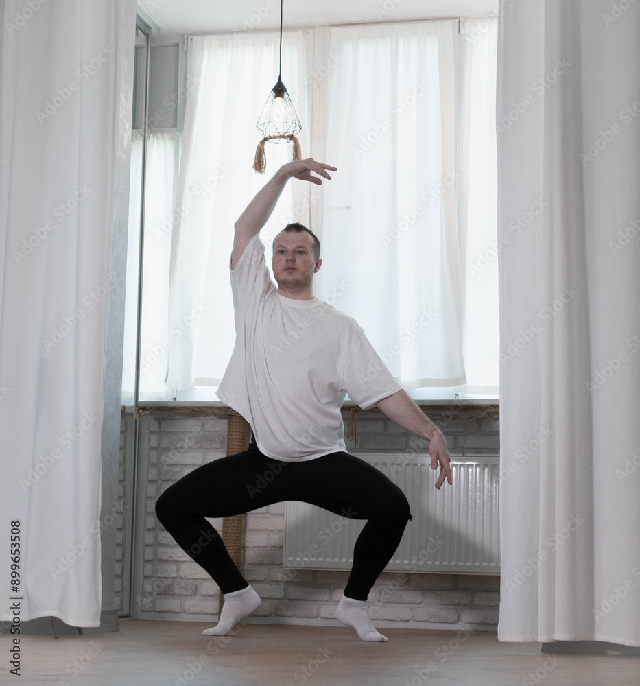 A young and handsome classical dancer is warming up in the apartment. Workout at home. Body stretching. A young and handsome classical dancer is warming up in the apartment. Workout at home. Body stretching.
