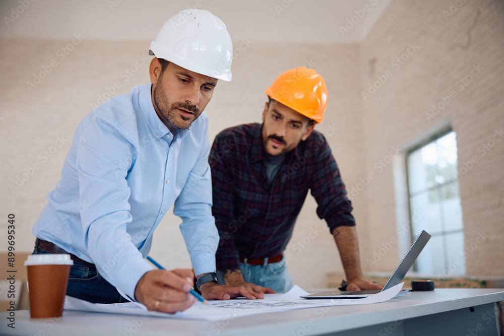 Housing project manager examining blueprints with construction worker during house remodeling. Housing project manager examining blueprints with construction worker during house remodeling.