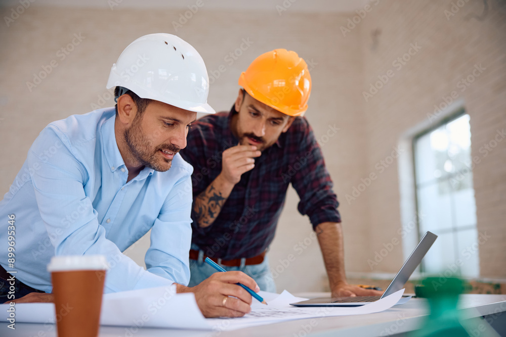 Smiling architect and construction worker analyzing blueprints during house remodeling. Smiling architect and construction worker analyzing blueprints during house remodeling.