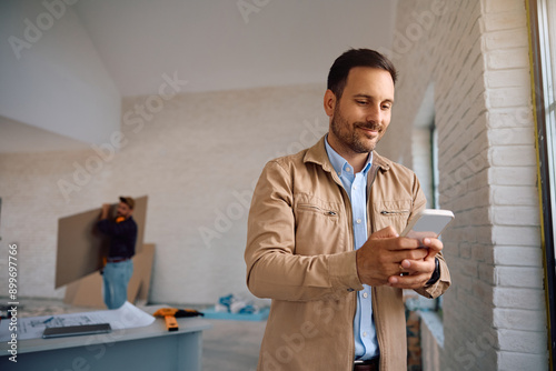 Smiling man using mobile phone during construction works at his house. photo