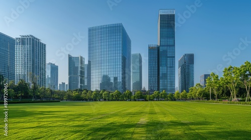 Tall company buildings aligned in the middle under a clear blue sky, with a front view of short green grass, devoid of any people.