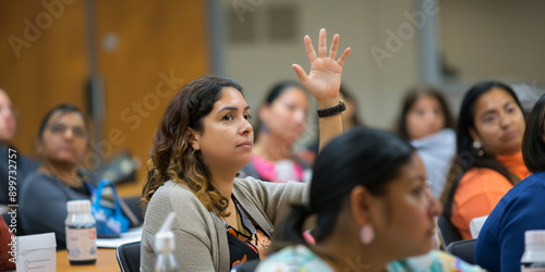 hispanic woman raises her hand in a classroom setting, asking a question to the lecturer or teacher.