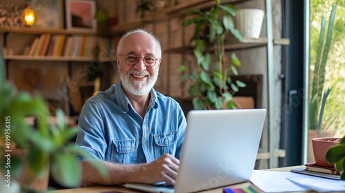 Cheerful senior man working on laptop at home office with bright smile. Mature businessman working remote from home with laptop and files.