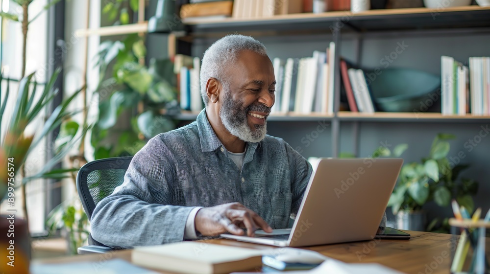 Cheerful senior man working on laptop at home office with bright smile. Mature businessman working remote from home with laptop and files. Cheerful senior man working on laptop at home office with bright smile. Mature businessman working remote from home with laptop and files.
