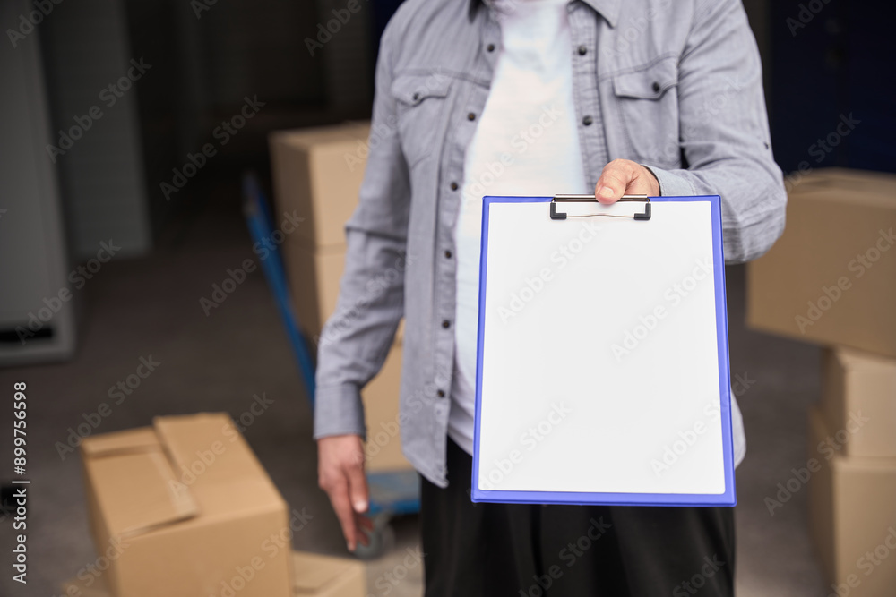 Worker with clipboard by stacked trolley of boxes Worker with clipboard by stacked trolley of boxes