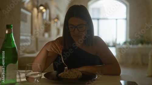 Beautiful young hispanic woman eating pasta in an italian restaurant with an elegant indoor setting and stylish decor photo