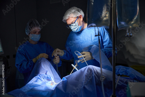 Male gynecologist with woman assistant in mask and hair cap with patient in gynecology chair. Hysteroscopy operation