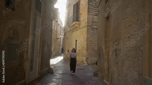 A young hispanic woman smiling and walking through the picturesque stone alleyways of lecce in puglia, italy, radiating joy amidst historic buildings.
